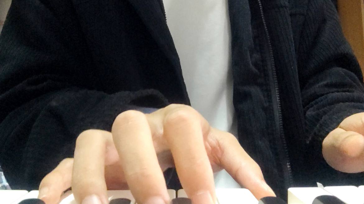 Close-up of a person in a dark jacket playing a piano keyboard.