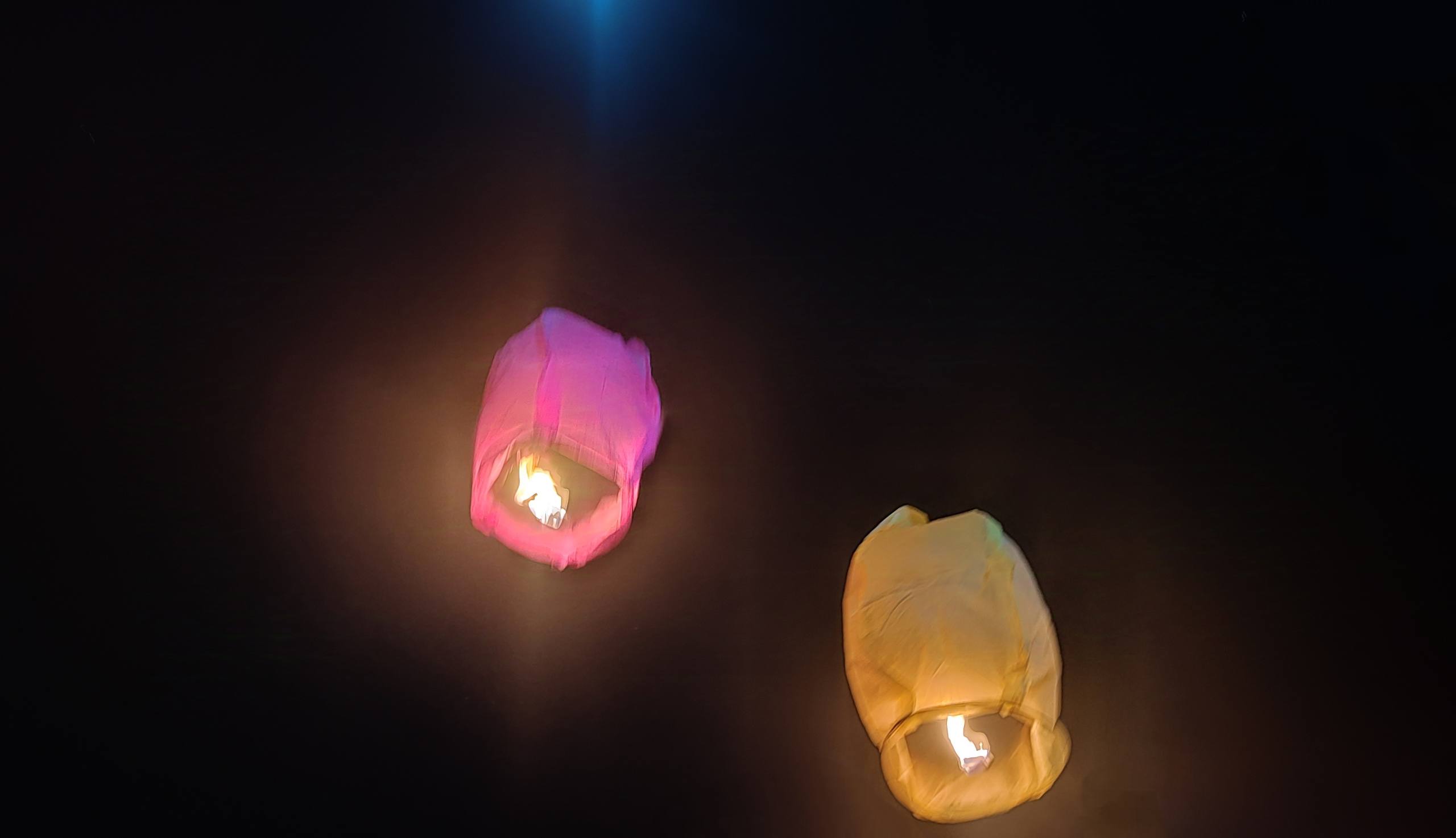 Two glowing sky lanterns, one pink and one yellow, floating against a dark night sky.