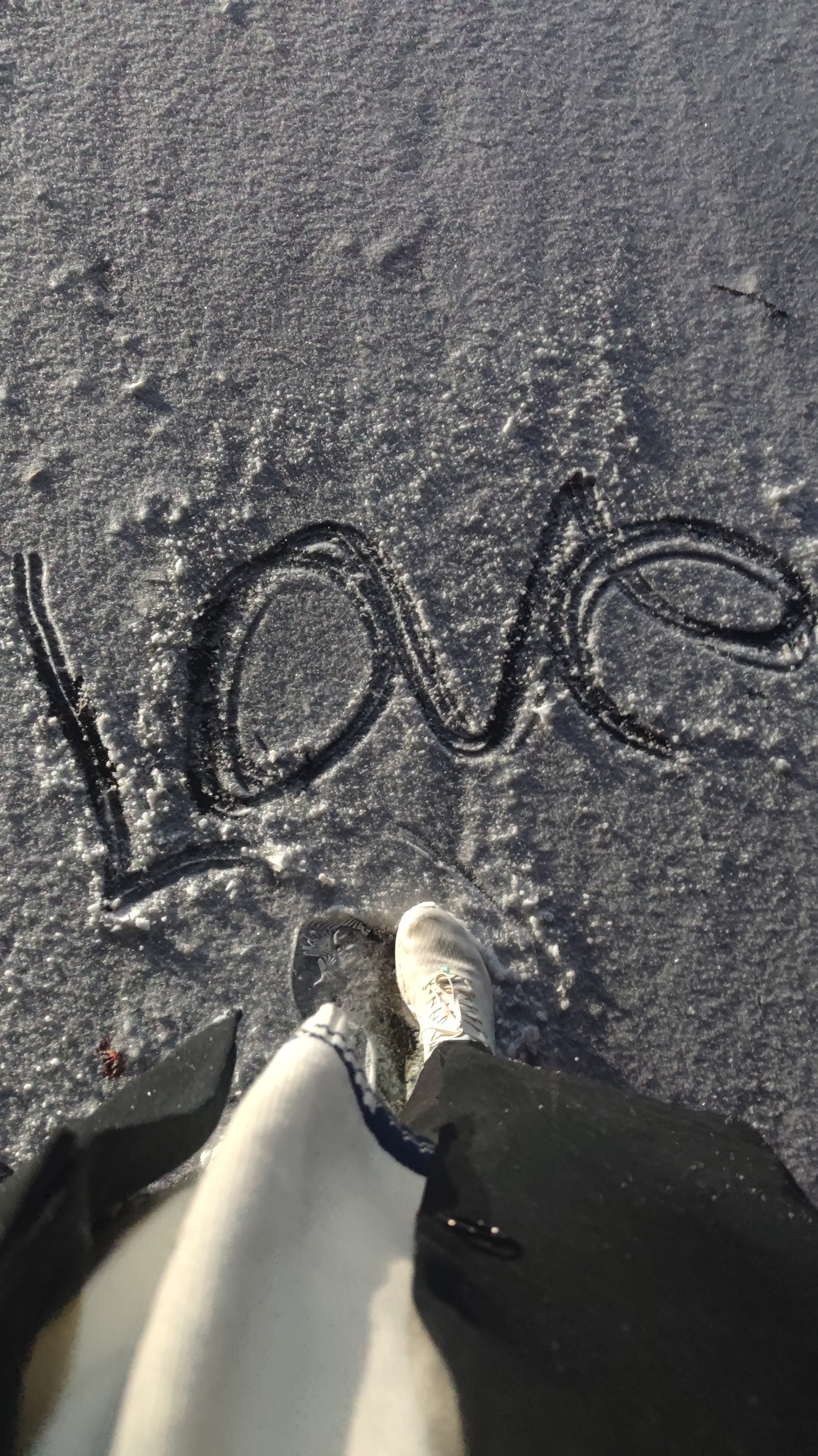 Top-down view of a person in a white sneaker standing on a frosty surface with the word Love written in large script across the ice.