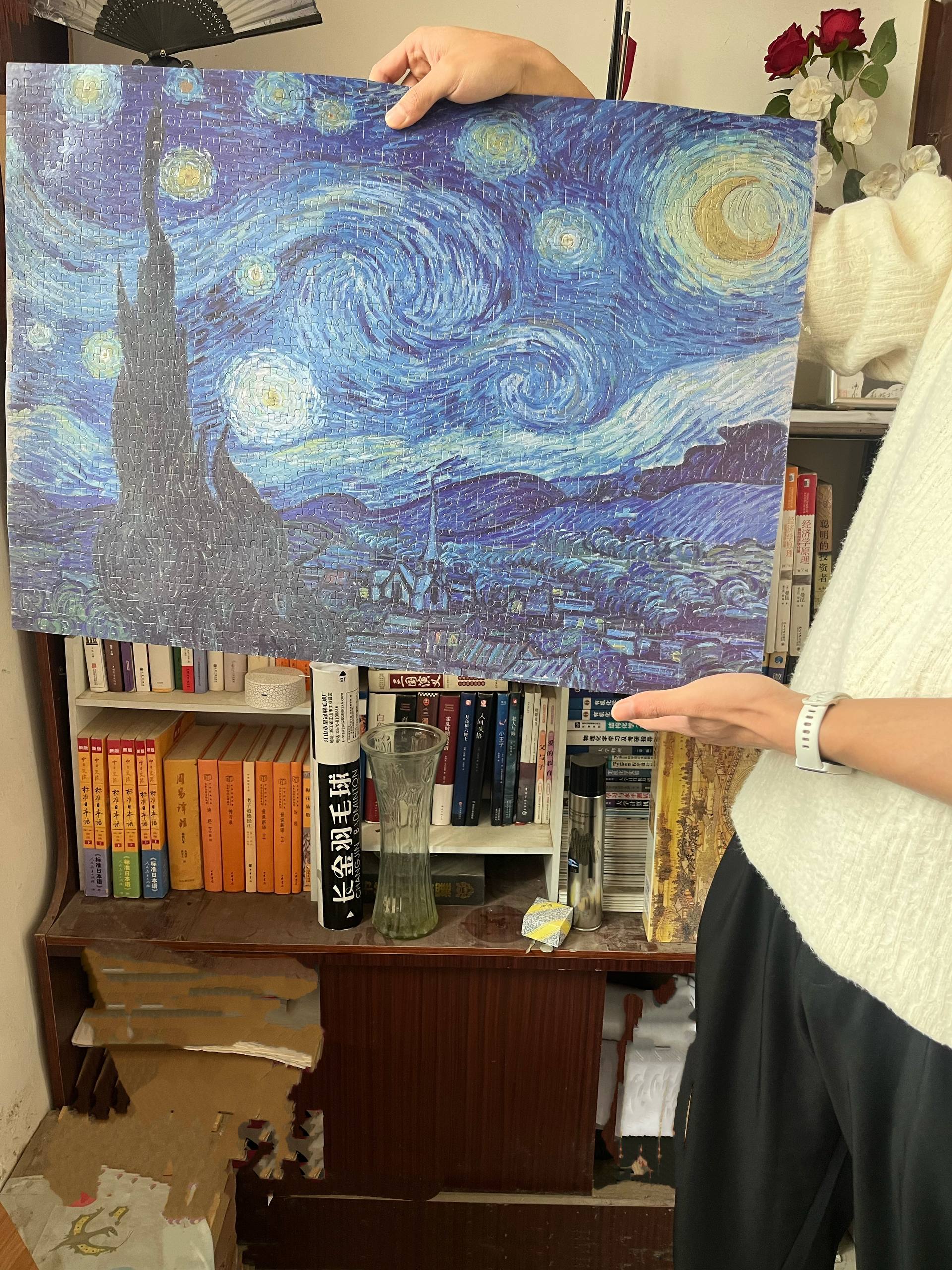 A completed Starry Night jigsaw puzzle held up in front of a bookshelf.