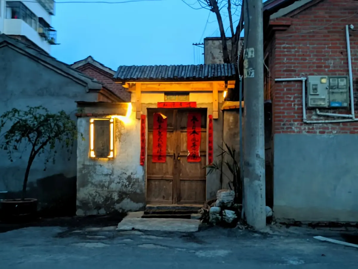 A small doorway with warm lights beside a brick wall in the evening.
